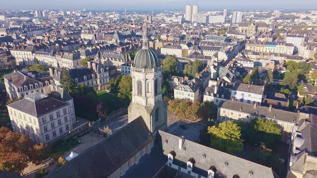 High-angle establishing shot showcasing the dome and tower of the historic Notre-Dame-en-Saint-Melaine Church dominating the densely packed urban architecture of the Rennes cityscape.