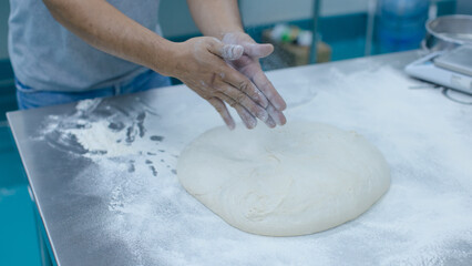 Unknown hand people knead fresh dough on floured stainless steel table in clean food preparation area, Factory production line baking preparation professional kitchen workflow industrial technology.