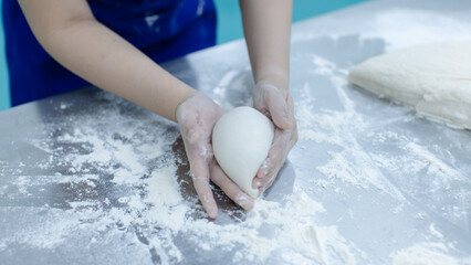 Unknown hand people knead fresh dough on floured stainless steel table in clean food preparation area, Factory production line baking preparation professional kitchen workflow industrial technology.
