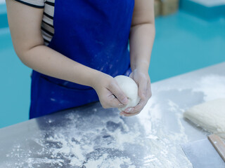 Fototapeta premium Unknown hand people knead fresh dough on floured stainless steel table in clean food preparation area, Factory production line baking preparation professional kitchen workflow industrial technology.