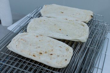 Freshly baked pizza rectangular flatbreads rest on stainless steel cooling rack light golden spots soft texture clean, professional baking workflow environment production process technology factory.