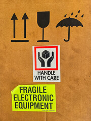 Close-up of a brown cardboard box with multiple shipping labels and symbols indicating fragile electronic equipment, handle with care, keep dry, and this way up.