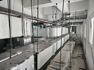 Long view of an industrial utility room filled with extensive insulated HVAC ducts and various suspended electrical conduits and piping systems.