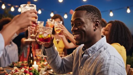 Happy african american man laughing at a backyard dinner party with friends at night under string lights in an outdoor setting. - Powered by Adobe