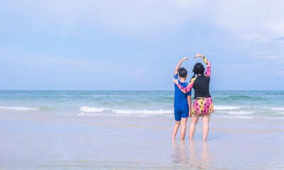 Asian mother and son forming a heart shape with their arms at the beach