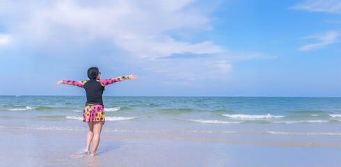 Asian woman in swimsuit standing arms open on the beach