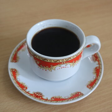 A cup of black coffee in a traditional ceramic cup with a matching saucer on a wooden table, perfect for themes of morning routine, caffeine, and warm beverages.