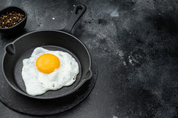 Sunny fried egg cooking in black skillet, crisp edges and glowing yolk. Minimal gourmet breakfast shot with strong texture detail.