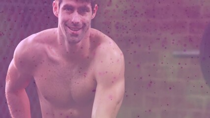 Man reaching shorts, adjusting, preparing kettlebell on gym floor, purple overlay tinting frame