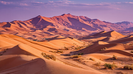 Naklejka premium Vibrant orange sand dunes under a purple sky landscape desert terrain with scattered vegetation and winding tracks leading through arid wilderness during sunset scenery