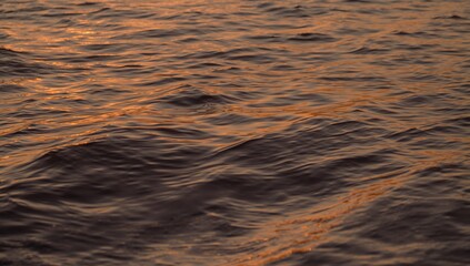 Rippling sea surface showing warm golden reflections at sunrise, featuring waves and ripples