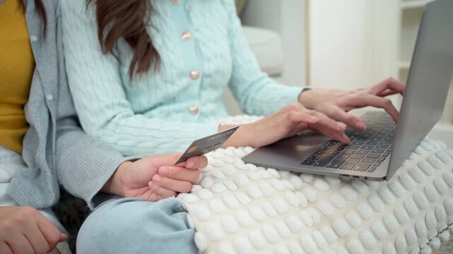 Two women shopping online with laptop and credit card at home.
