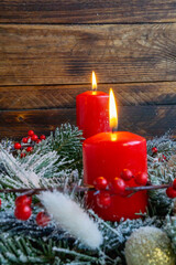 Two glowing red candles in snowy evergreen wreath