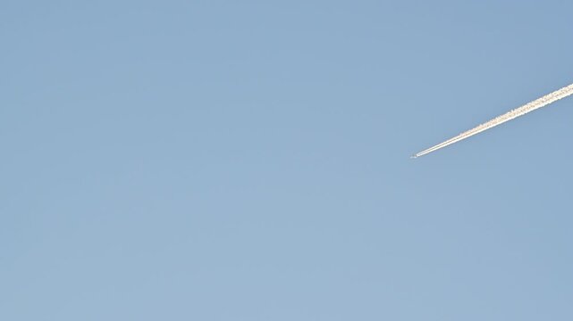 Airplane flying high up in the sky leaving a vapor trail in the clear blue sky.