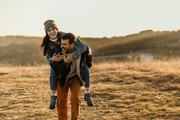 Happy couple enjoying piggyback ride in nature at sunset