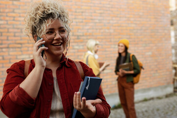 Smiling female student talking on phone at campus