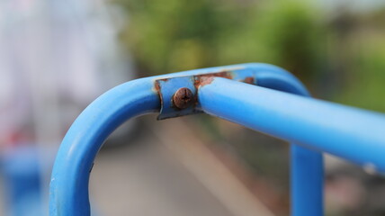 Close-up View of Rusty Blue Metal Bar on Playground Equipment Surrounded by Greenery