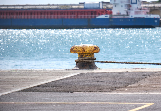 Massiver Poller mit Tauen an einer Kaimauer am Ufer im Industriehafen Isle of Portland in Gro&szlig;britannien, mit Schiff im Hintergrund und Sonnenreflexionen im Wasser, Copy Space