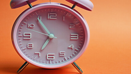 Pink alarm clock on orange background 