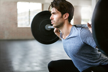 Strong, weightlifting and man squat with barbell in gym for exercise, bodybuilder training and workout. Serious, sports and person with weights for muscles, strength and challenge for fitness