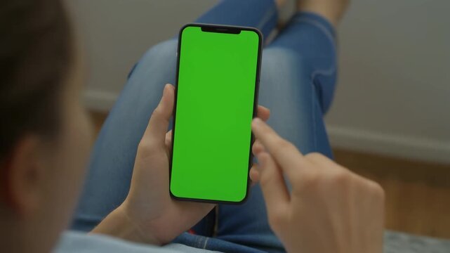 Female hands interacting with a chroma key green screen mobile phone, swiping and tapping. Ideal for digital advertising, technology projects, and app mockups.