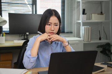 Serious Asian female office worker thinking and analyzing data while looking at her laptop screen
