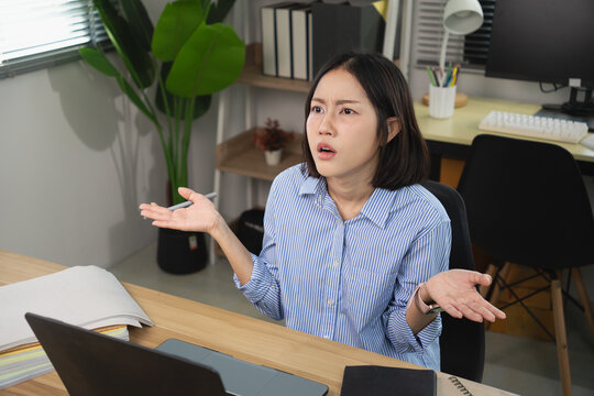 Confused Asian female office worker expressing frustration and shrugging at her desk