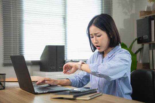 Shocked Asian female employee looking at her watch due to a tight deadline or urgent task