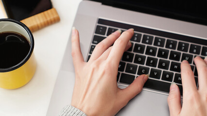 Close-up top view of woman hands typing on a laptop keyboard, focusing on digital workspace, symbolizing work, study, and modern online communication.
