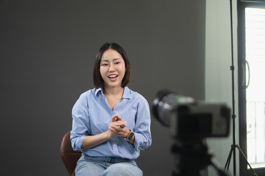 Young Asian woman smiling and talking to a camera during a video interview in a professional studio