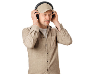 A man in a cap and a button-up shirt stands and listens to music through headphones. He appears focused and engaged with the sound.