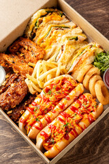A high-angle close-up shot of a fast-food delivery box filled with various items: hot dogs, french...