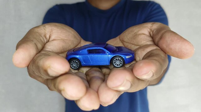 Closeup of hand holding toy car on palm. New vehicle online loan or insurance purchase scam on digital automobile marketplace concept. Automotive part internet buying and selling business scam warning