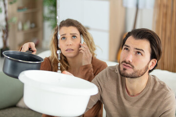 emotional couple collect water leaking from ceiling while phoning plumber