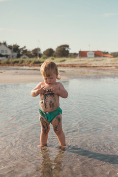 Toddler boy playing with mud in water at beach