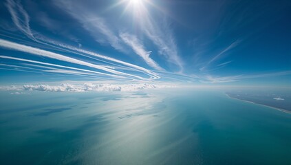 Displaying expansive seascape centered over ocean, showing sun, contrails, cirrus, sandy coastline