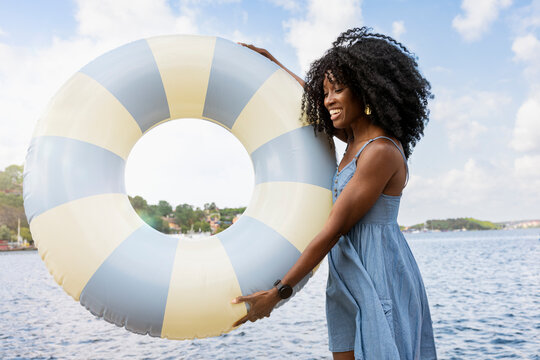 Smiling woman with curly hair holding swimming float near river