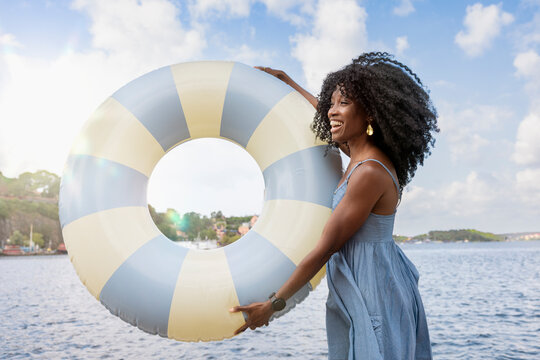 Happy woman holding swimming float near river