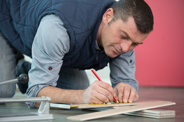 tradesman laying flooring measuring plank of wood