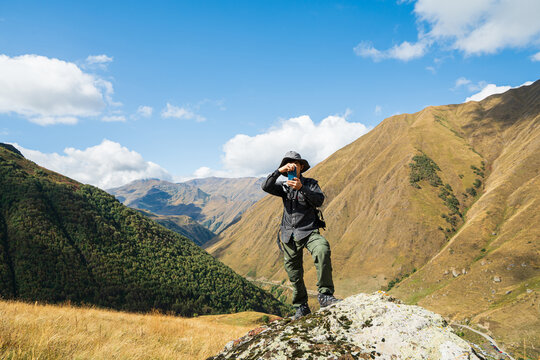 Successful hiker taking a photo on a rocky peak in Juta Village, Georgia. Mountain climbing adventure with panoramic views, sunny blue sky, and active outdoor lifestyle in the Caucasus Mountains.