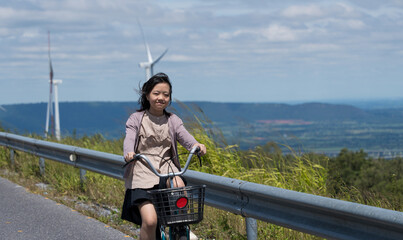 Happy Asian girl child cycling on countryside road under blue sky, symbol of green and renewable energy.