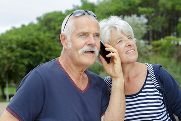 smiling senior couple listening to conversation from smartphone