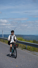 Young Asian boy biking along rural road beside wind turbines on a sunny day.