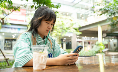 A young girl using her smartphone with a drink on the table in a bright open area.