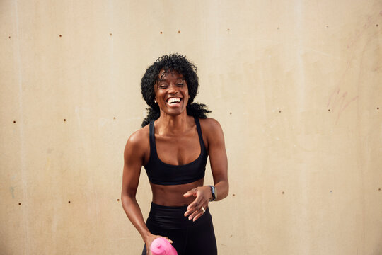 Portrait of happy female athlete laughing against wall at park