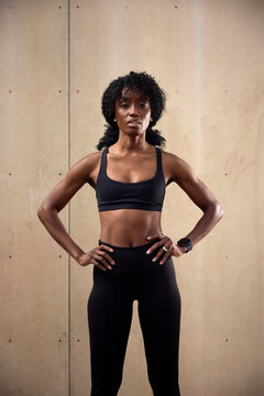 Portrait of confident female athlete standing with arms akimbo against wall