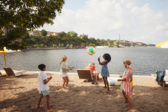 High angle view of family friends playing throw and catch ball on beach
