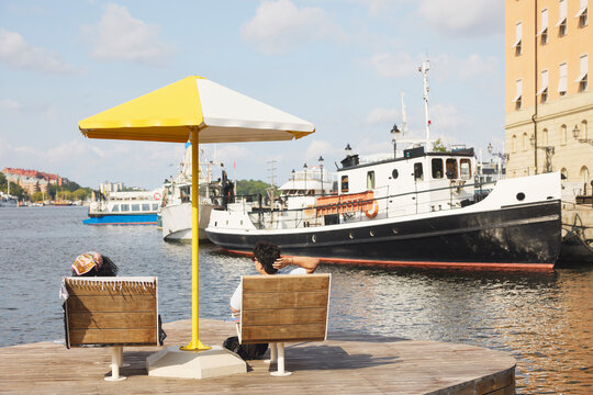 Rear view of male and female friend spending leisure time under beach umbrella amidst river