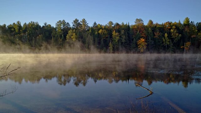 Cinematic nature shot of mist drifting above the Au Sable River at dawn.