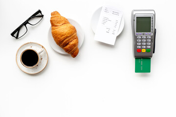 Bank card payment POS terminal. Paying the bill at a restaurant. Cup of black coffee with the bill on white table.